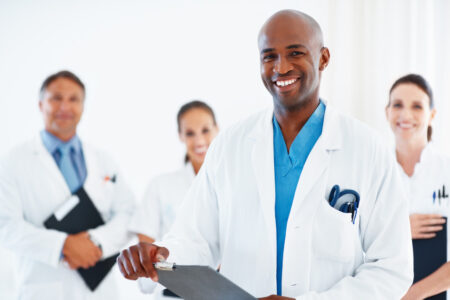 Portrait of happy young male doctor holding medical reports with team in background